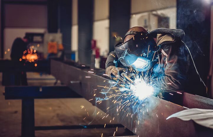 A welder fabricating a structural steel member, sparks flying